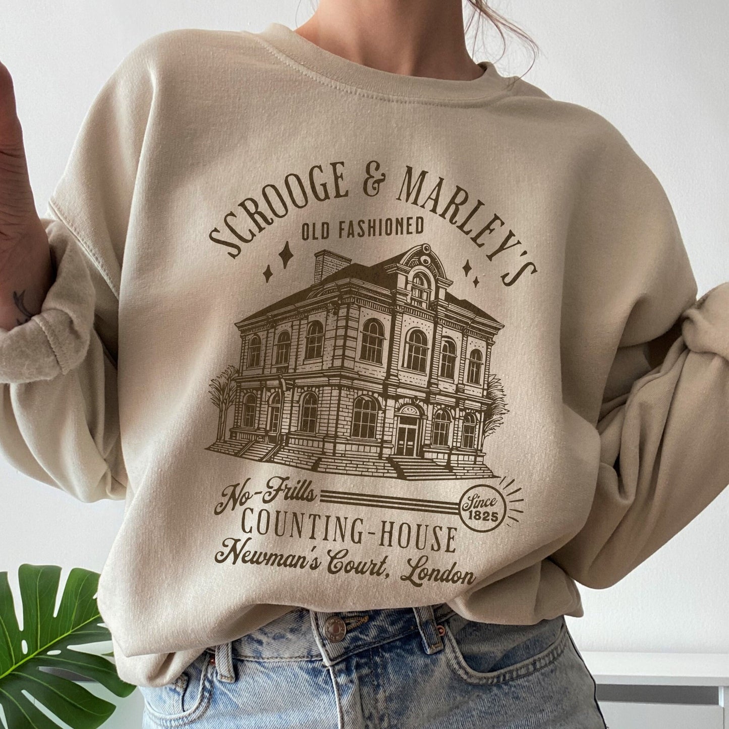 May include: A beige sweatshirt with a brown graphic print of a building with the text &#39;SCROOGE & MARLEY&#39;S OLD FASHIONED&#39;, &#39;No-Frills COUNTING-HOUSE&#39;, &#39;Since 1825&#39;, and &#39;Newman&#39;s Court, London&#39;.